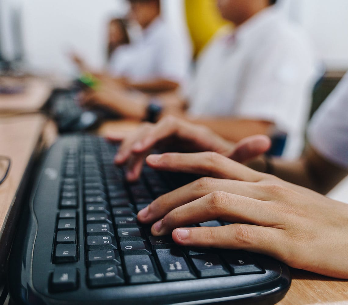 A group of students typing on a computer keyboard in a classroom setting.